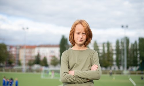 Ein Junge steht mit verschränkten Armen vor einem Fußballfeld