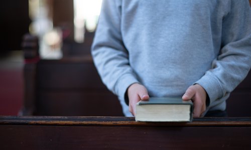 Ein Kind steht mit einer Bibel in der Hand zwischen Kirchenbänken 