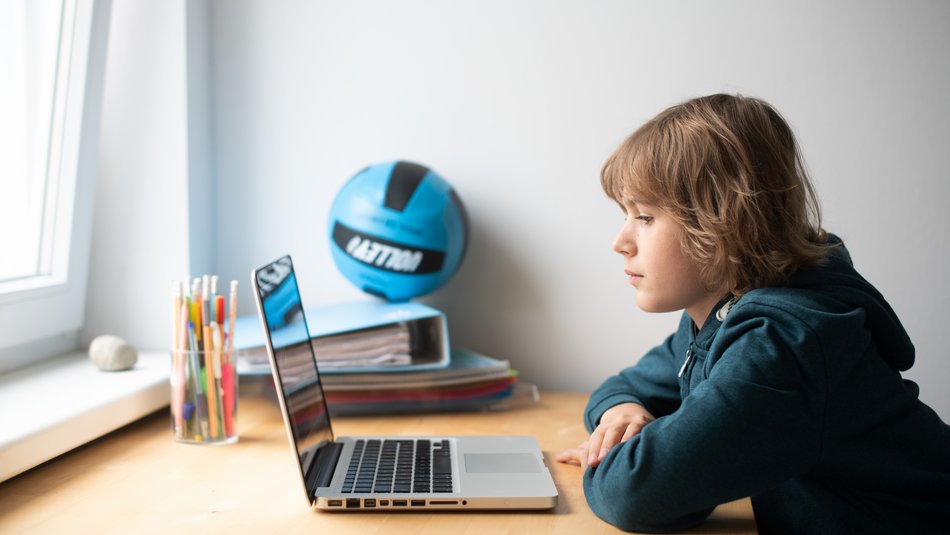 Ein Junge sitzt vor einem Laptop und schaut auf den Display