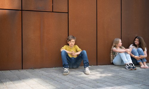 Ein Junge und zwei Mädchen sitzen vor einer Wand